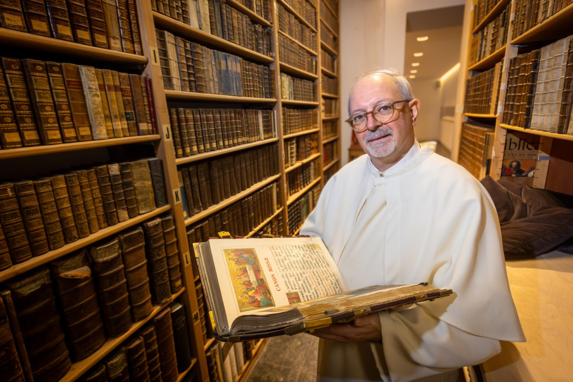 Pater Nicolaas houdt een geïllustreerd antiek boek vast in de bibliotheek van de abdij van Postel.