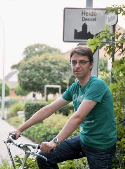 Diaken Jurgen Deckx (43) op de fiets bij een bord met plaatsnaam Heide Dessel.