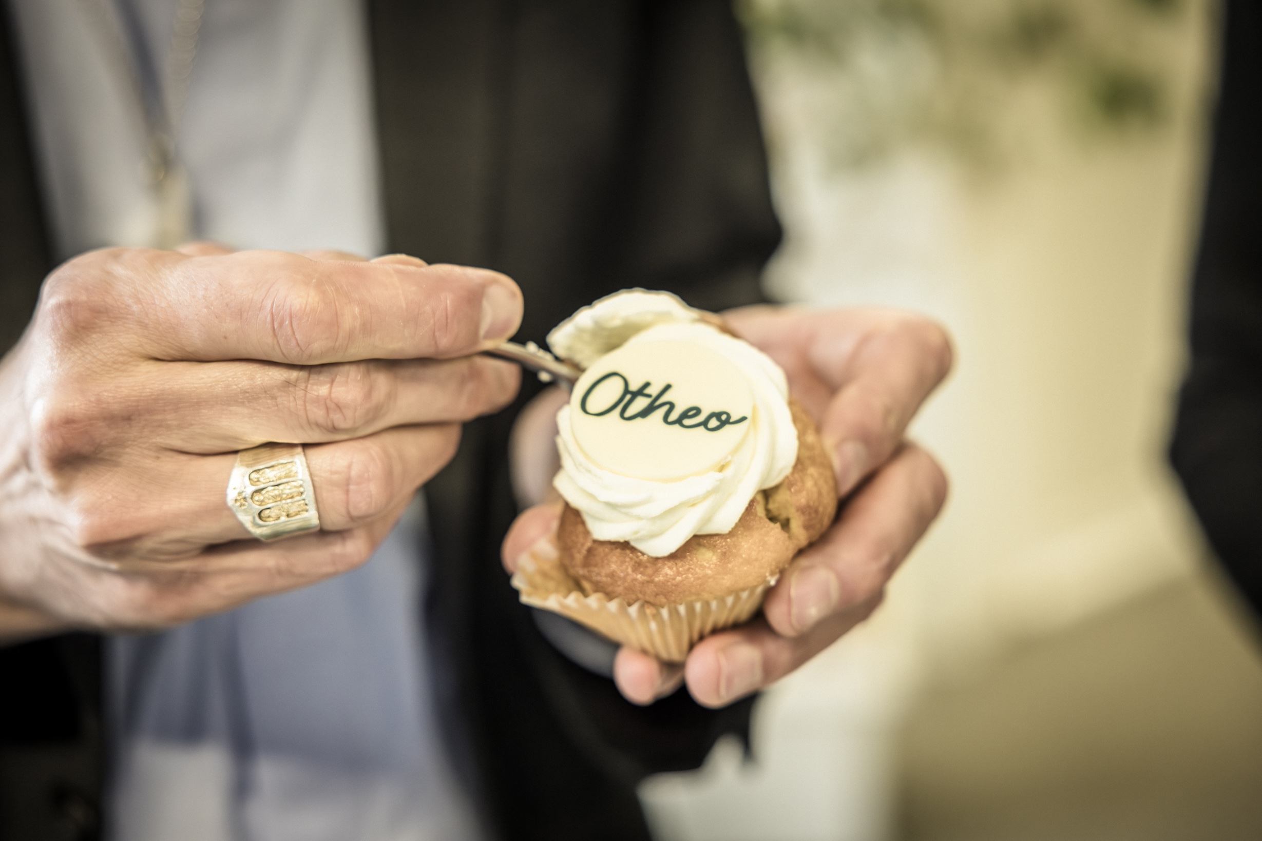 Aartsbisschop Luc Terlinden, te herkennen aan zijn bisschopsring, zet de vork in een cupcake met het nieuwe logo van Otheo.