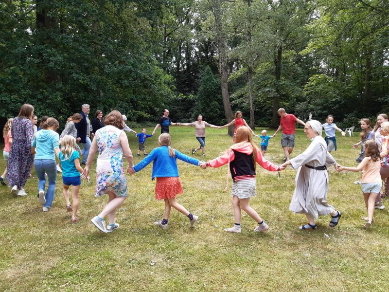 Ouders, kinderen en een zuster benedictines dansen in het rond. Foto van GezinStop-vakantie 2022.