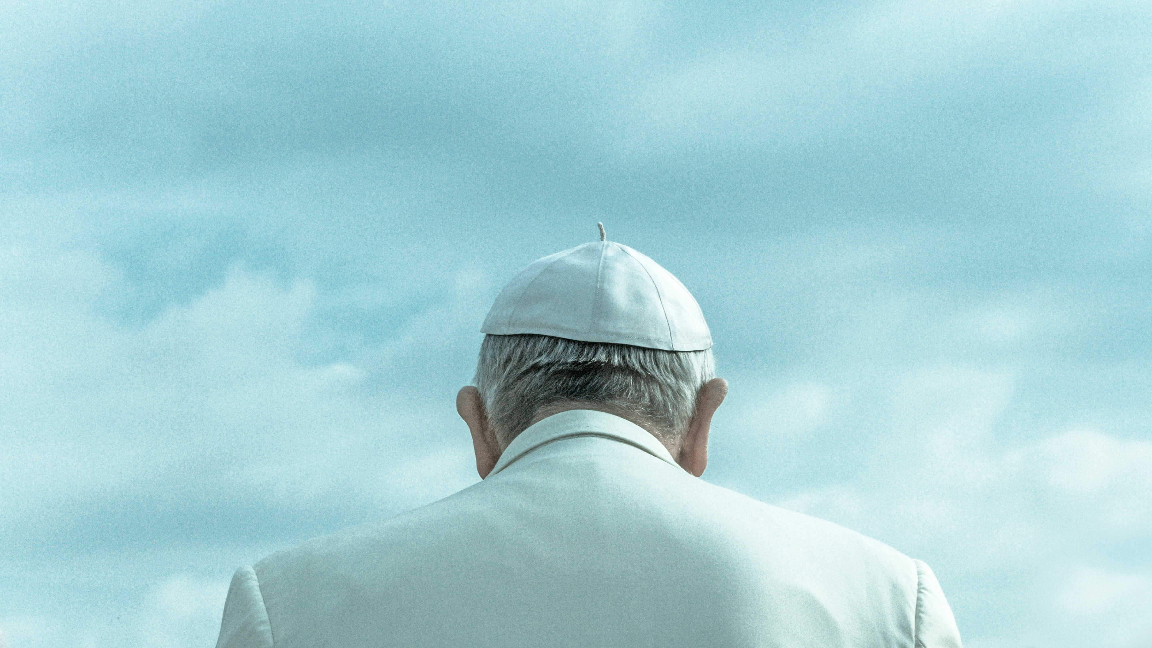 Paus Franciscus, foto van op de rug. Witte kledij tegen blauwe, bewolkte hemel.