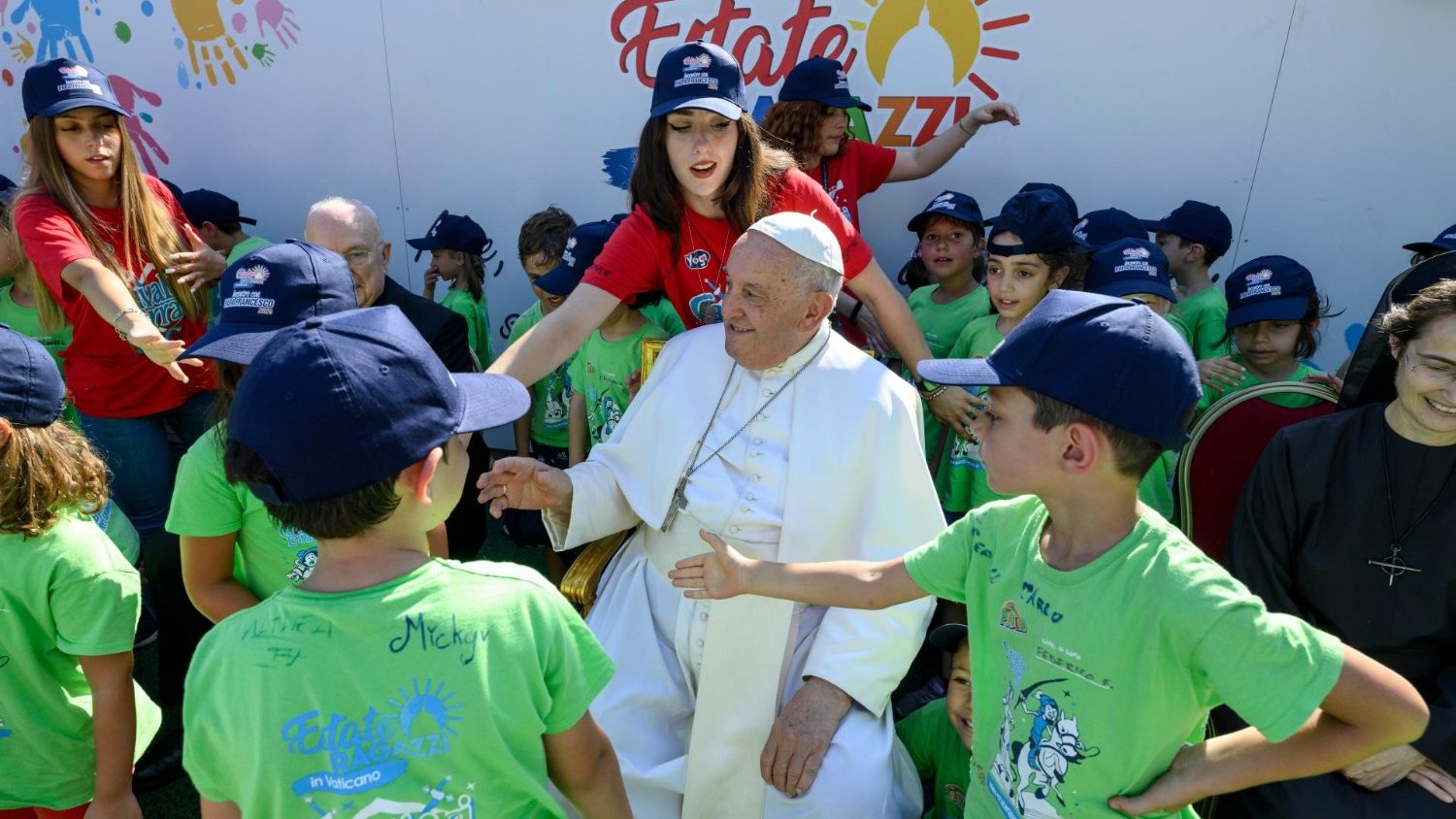 Paus Franciscus omringd door kinderen in groene T-shirts op het zomerkamp van het Vaticaan.