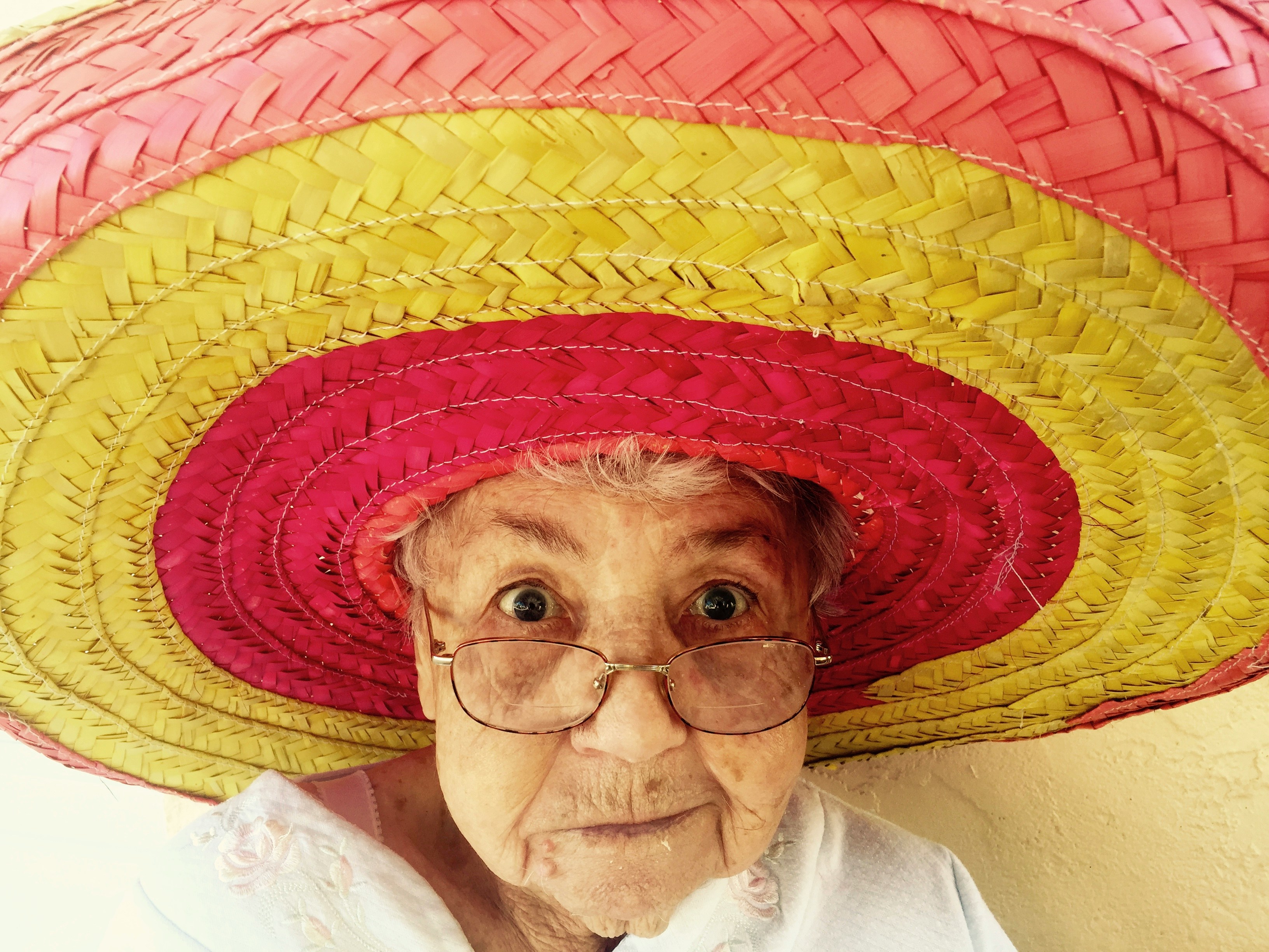 Oud vrouwtje kijkt ondeugend in de lens, met kleurige sombrero op het hoofd