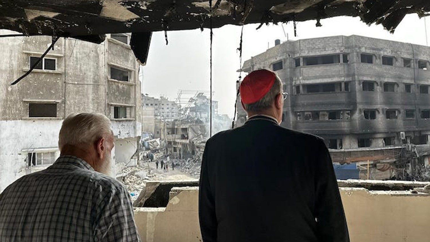 Kardinaal Pizzaballa (van op de rug) bekijkt de vernieling in de straten van Gaza, vanuit een kapot geschoten gebouw.