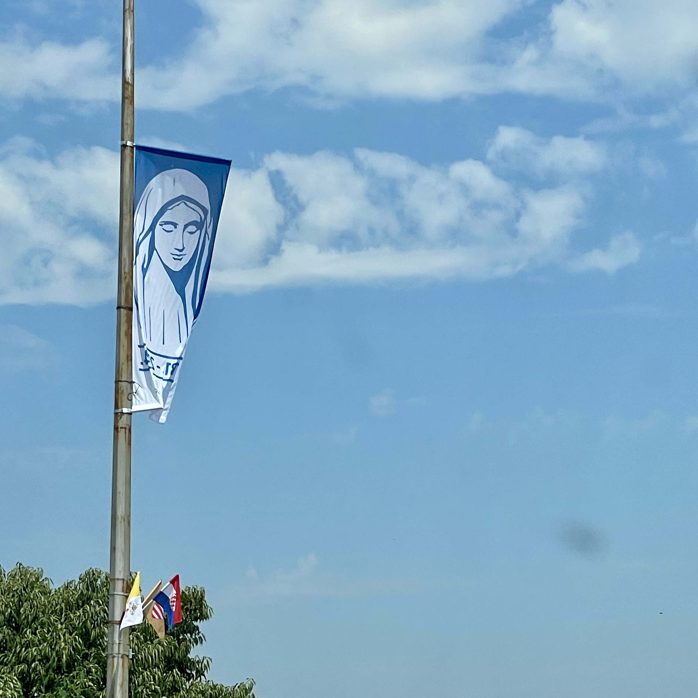 De vlag met het Mariabeeld van Medjugorje wappert tegen een straalblauwe hemel.