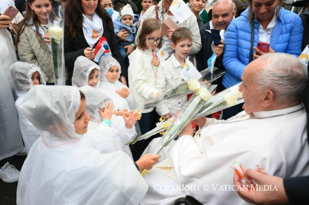 De paus begroet kinderen bij aankomst aan het Bisschoppelijk huis in Luxemburg, ontvangt bloemen en stopt hen een snoepje toe.