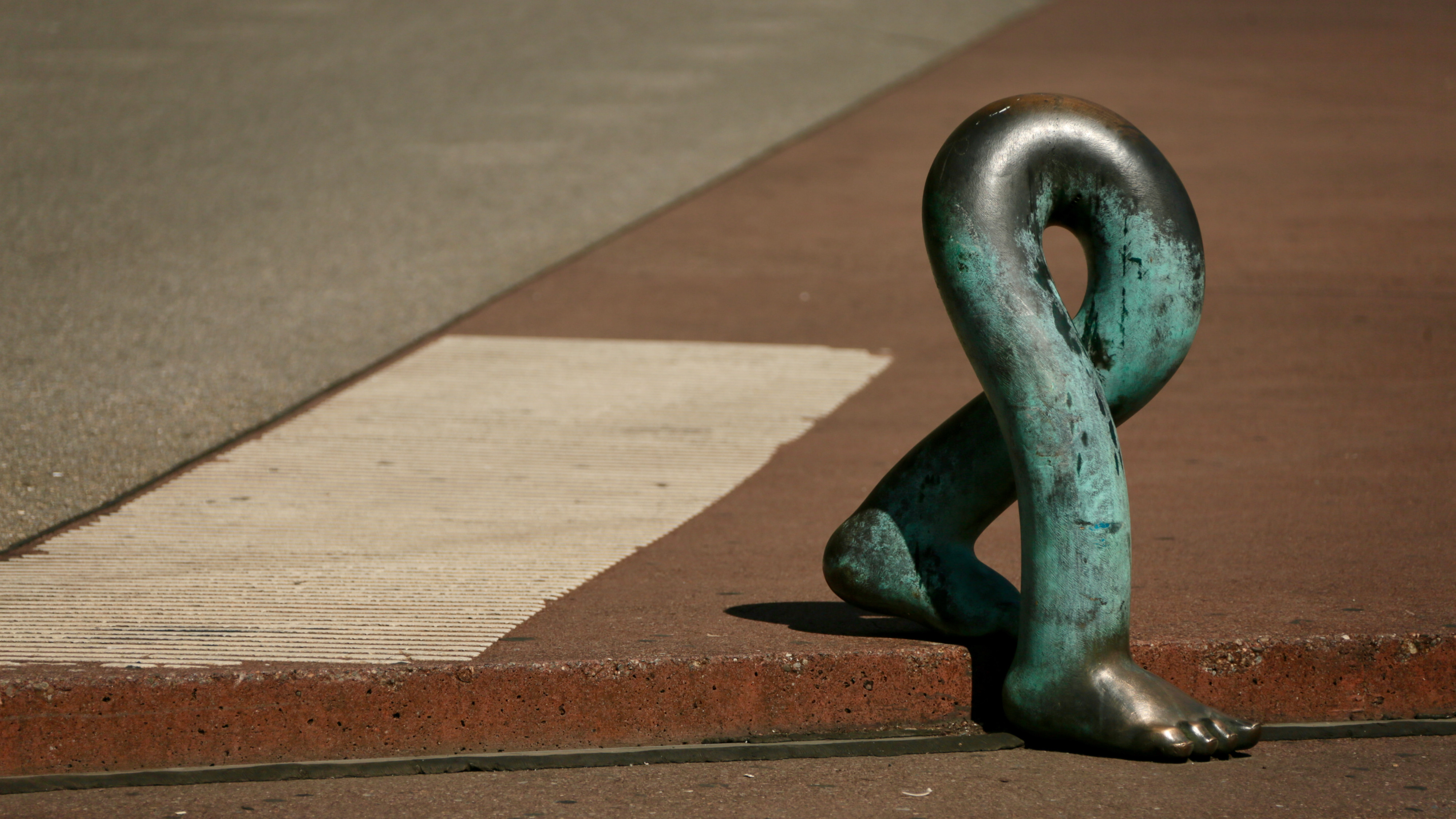 De foto tont een bronzen beeld van twee wandelende voeten op de weg.