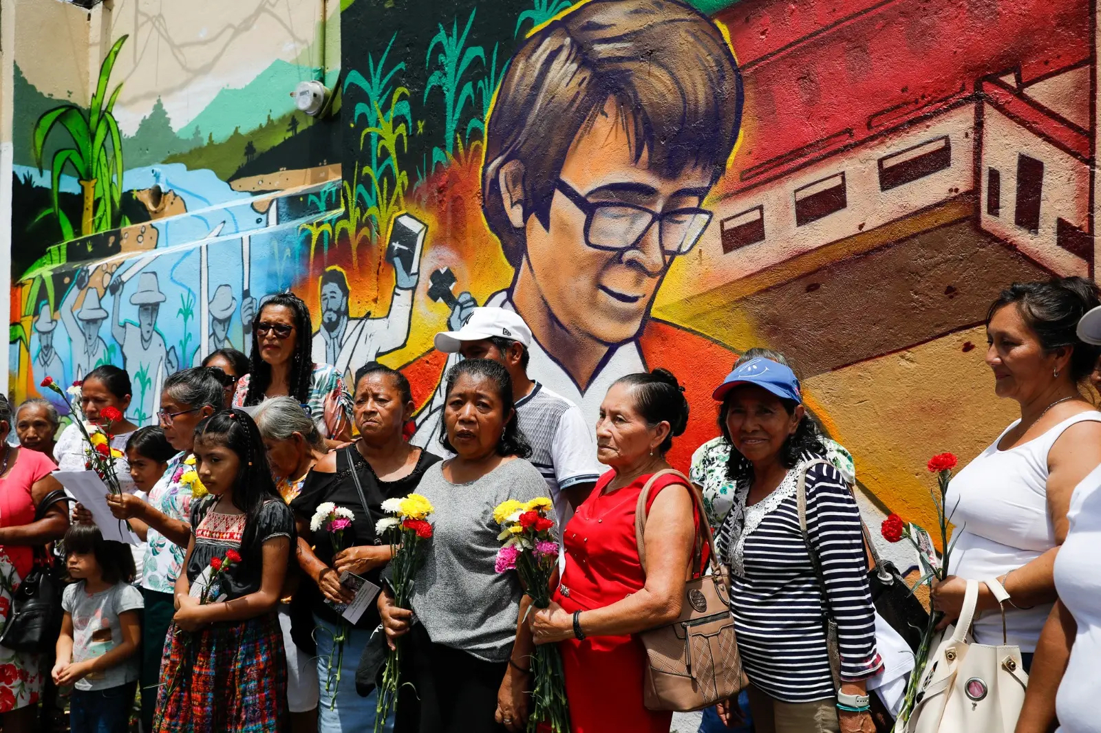 Vrouwen met bloemen poseren voor een muurschildering van scheutist Walter Voordeckers in Santa Lucia Cotzumalguapa in Guatemala.