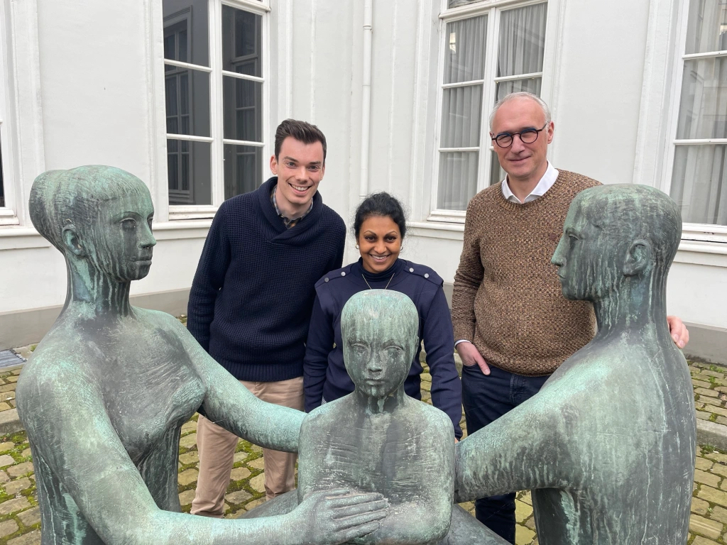 Voormalige collega’s Arno Gillemot, Beena Dockx en George Fleere van de pastorale dienst van AZ Monica bij een beeld van figuren in een kring.