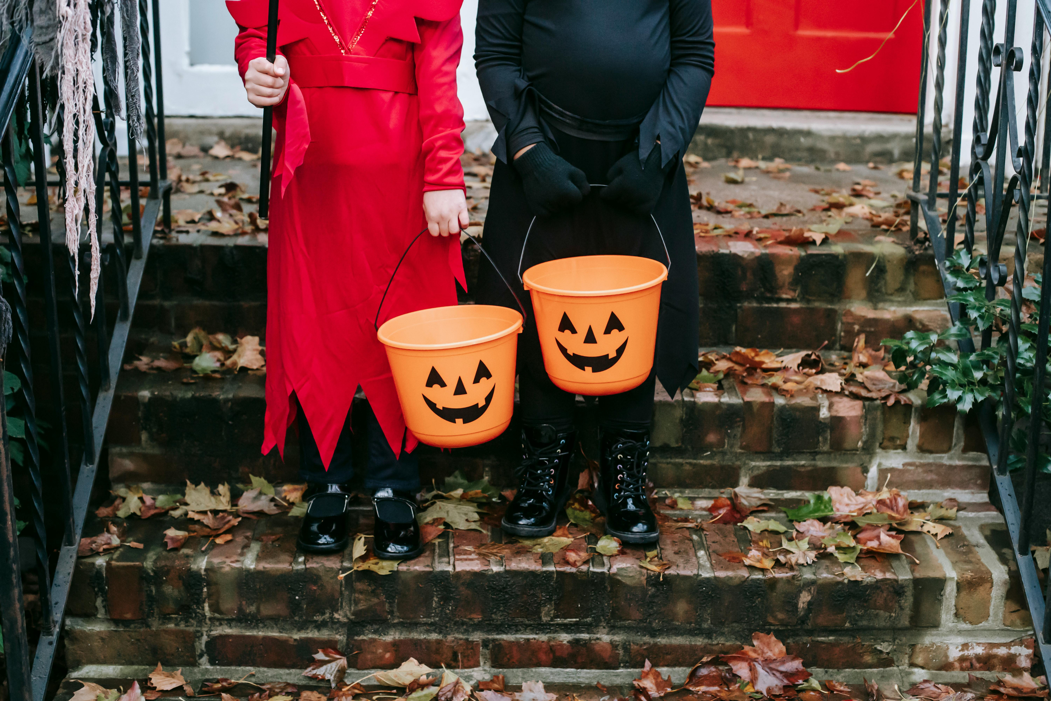 Twee kinderen staan met hun Halloweenemmertje op de trap, klaar om om snoepjes te gaan bedelen in de buurt.