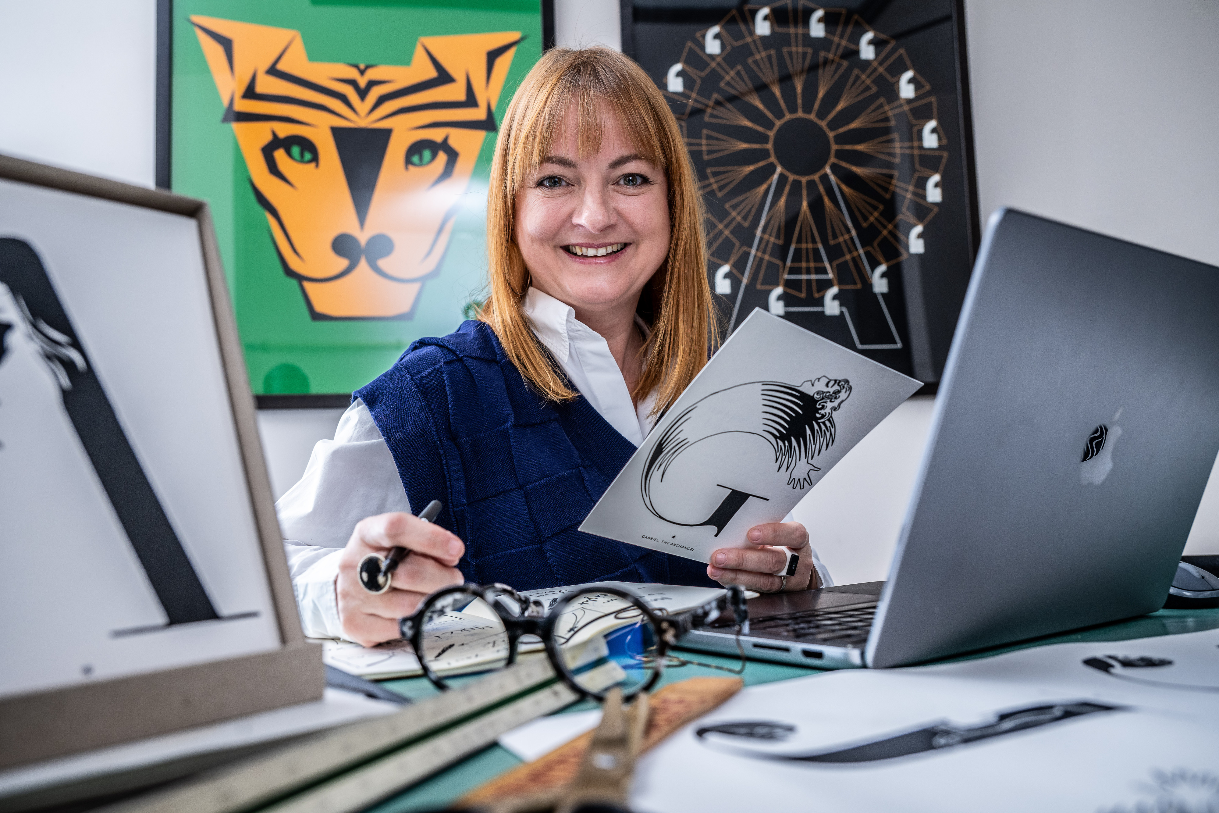 Sanny aan haar ontwerptafel met letterbeelden op de achtergrond.