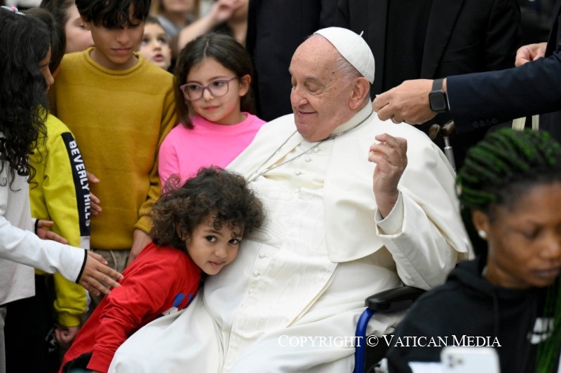 Een klein meisje vleit zich tegen de buik van paus Franciscus in zijn rolstoel.