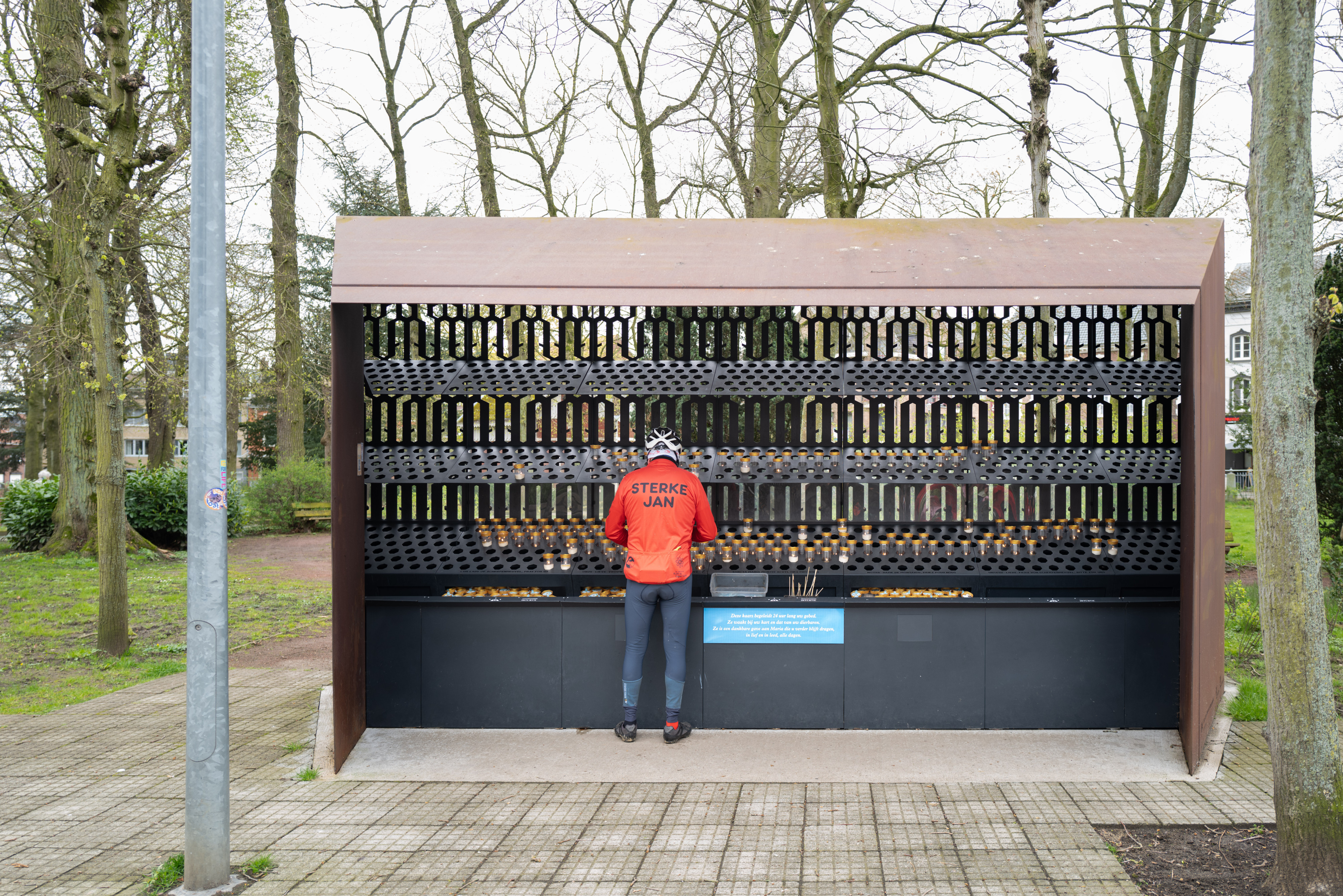 Man in fietstenue met opschrift 'Sterke Jan' steekt kaarsje aan in Scherpenheuvel.