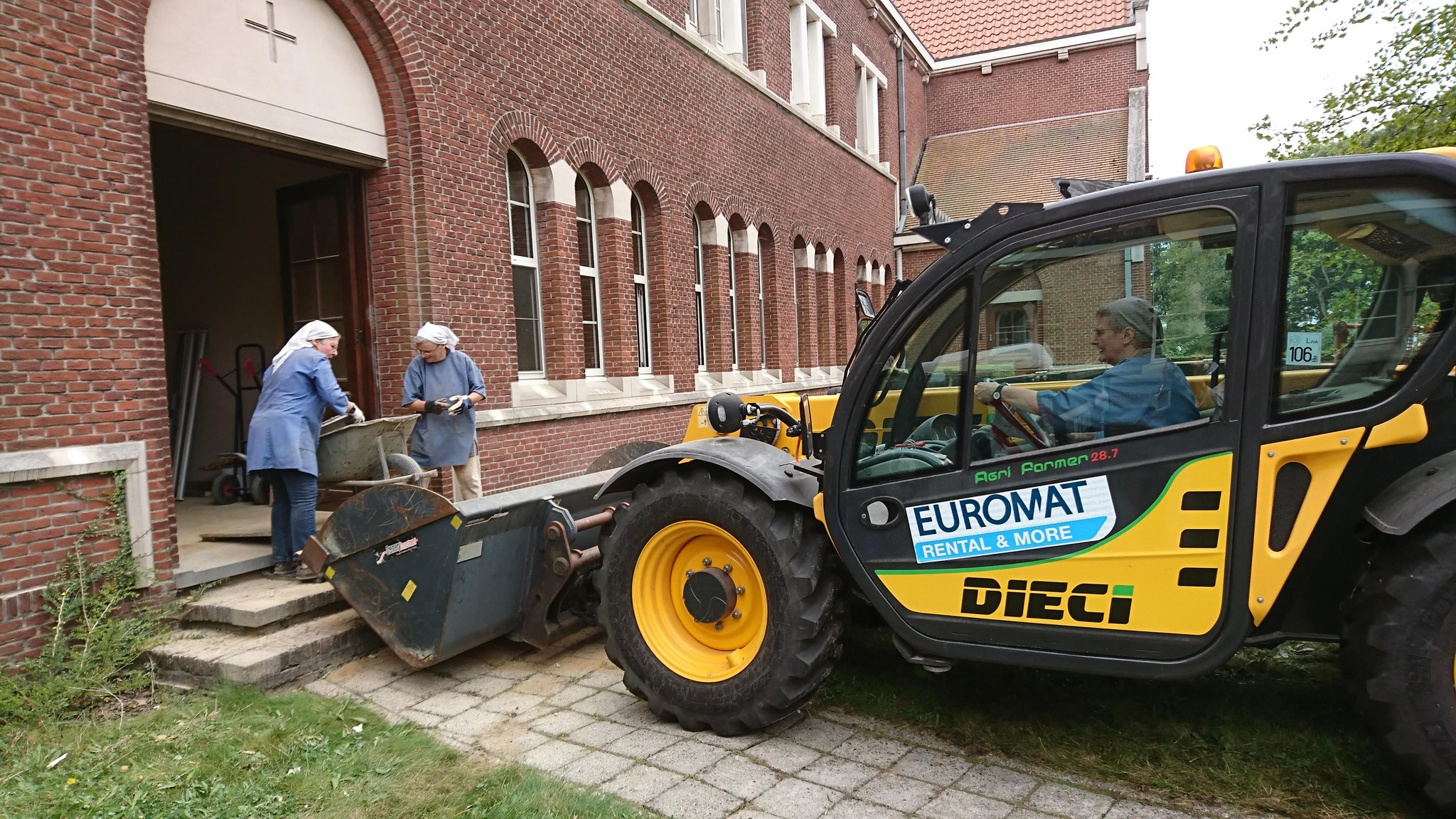 Twee zusters sjouwen met een kruiwagen, de derde bestuurt een zware machine..