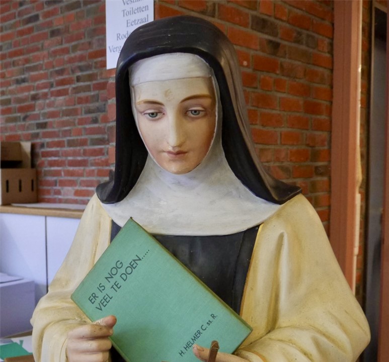 Sculptuur van een trappistin. In de handen is een boek gestopt met als titel 'Er is nog veel te doen'.