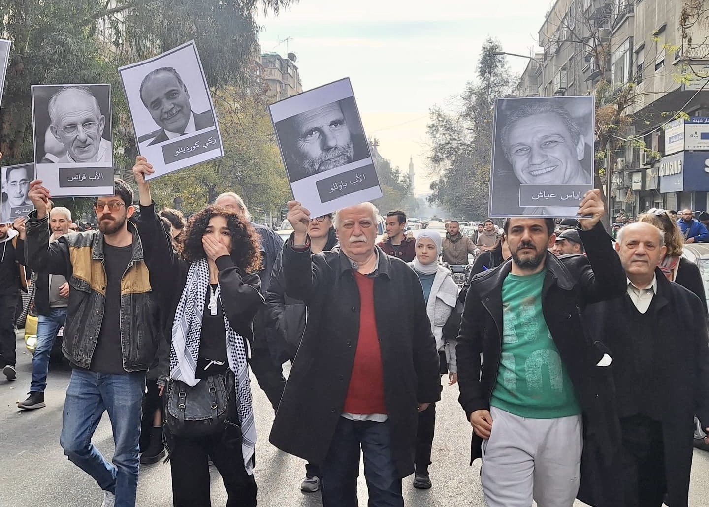 Betogers in Damascus steken portretten van vermisten in de lucht. In het midden een foto van Paolo Dall'Oglio.