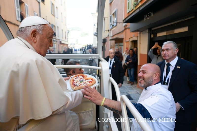 Pizzabakker overhandigt paus in pausmobiel een pizza in de vorm van een hart.