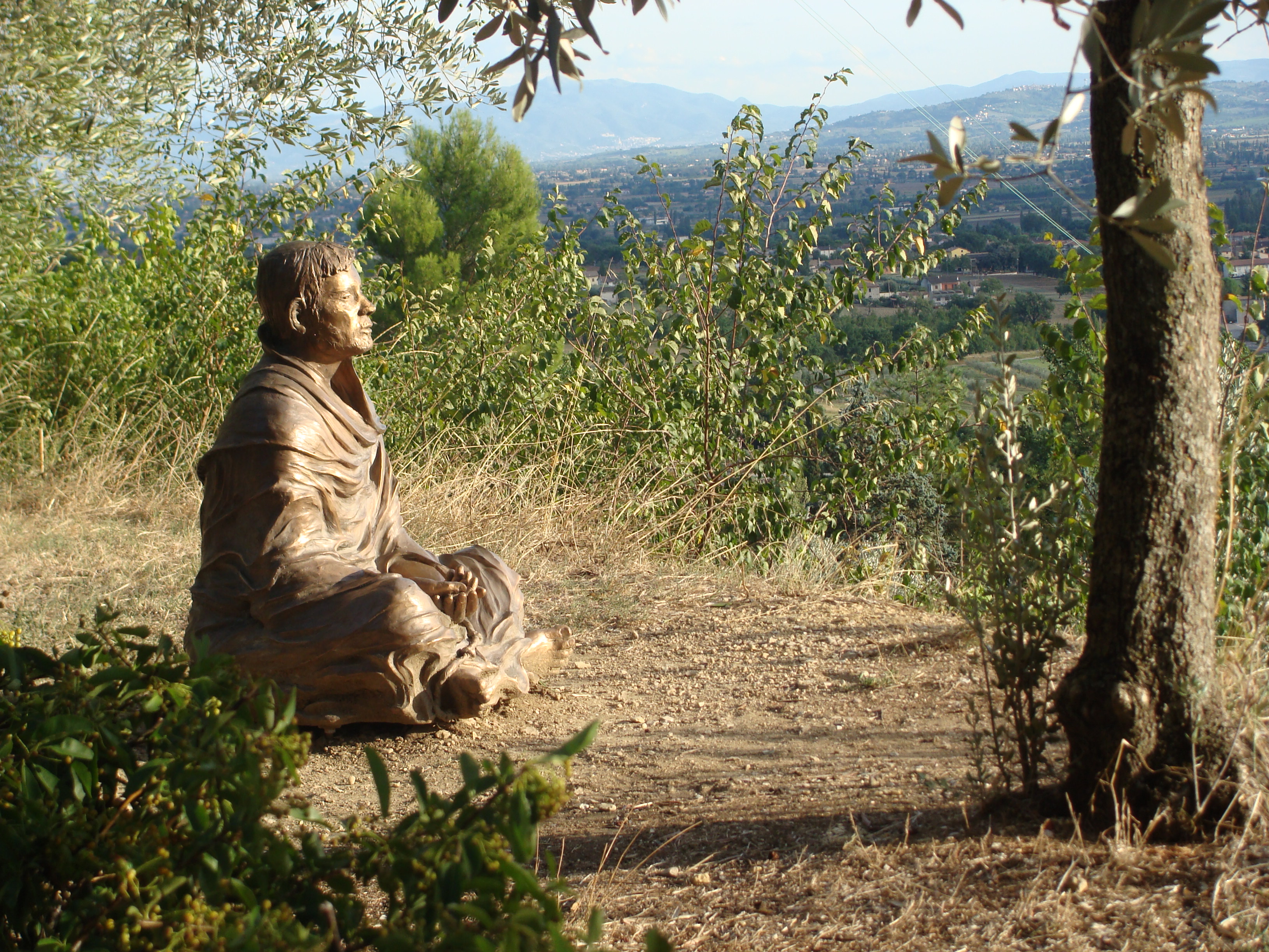 Beeld van Franciscus van Assisi in kleermakerszit uitkijkend over het landschap van op een berg.