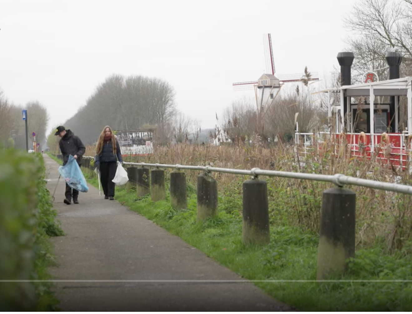 Twee jongeren pikken afval op langs een waterloop in Brugge.