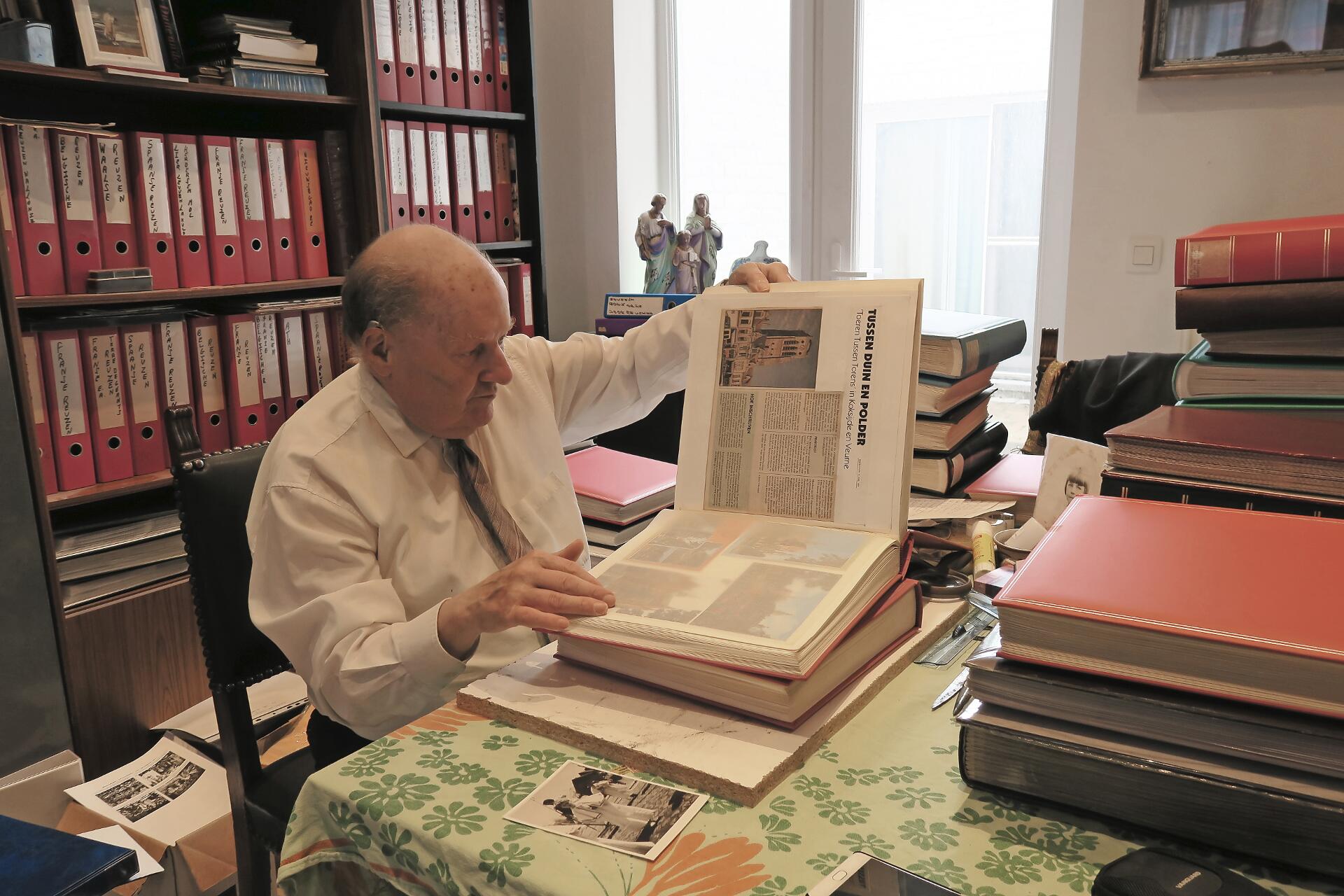 Paul De Jonghe op zoek in een van zijn talrijke boeken vol krantenartikels en foto’s. © Sien Wevers