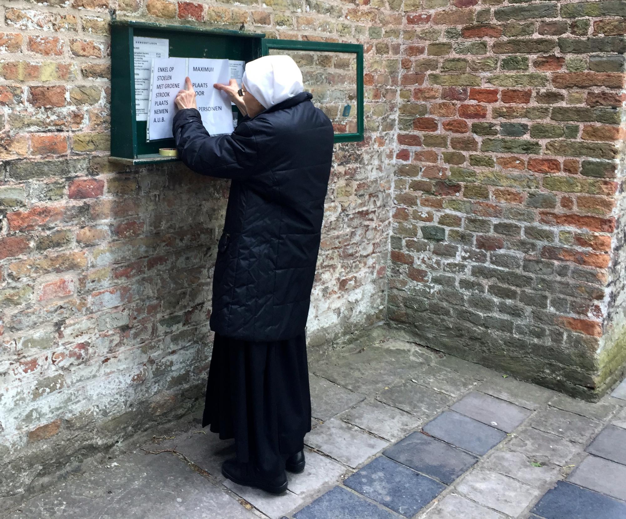 Een zuster hangt een blad met richtlijnen uit aan de Begijnhofkerk in Brugge.