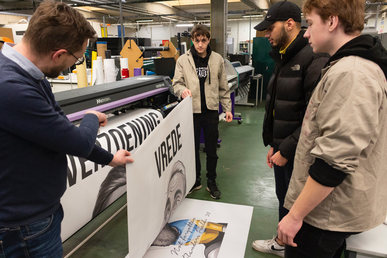 Enkele leerlingen en een begeleider tijdens een proefdruk van de banners.