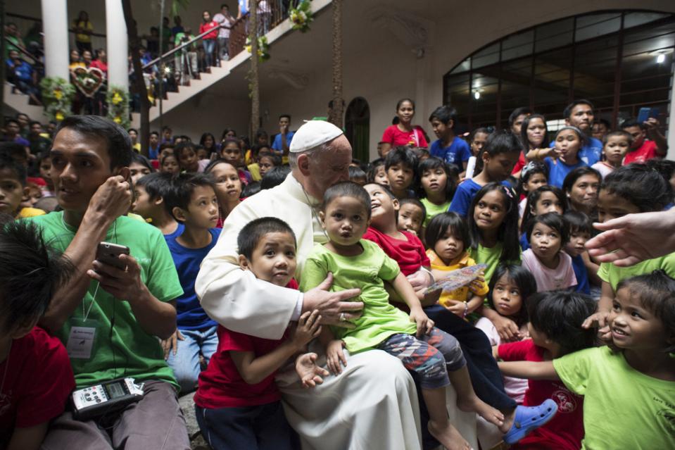 Paus Franciscus neemt kinderen uit een sloppenwijk in de Filippijnen op schoot.