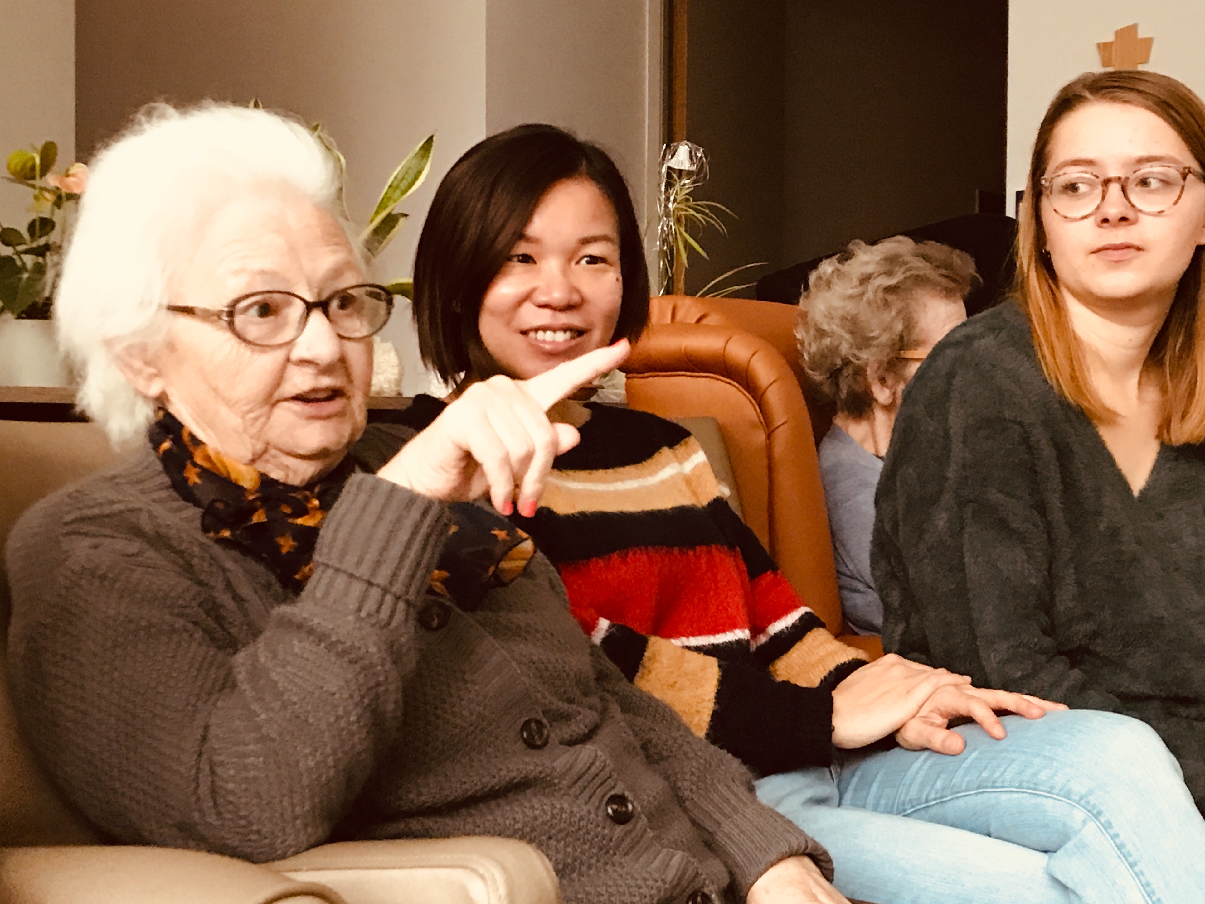 In de woonkamer zitten enkele ouderen gezellig bijeen. Ina en Pat schuiven mee in de fauteuil. 