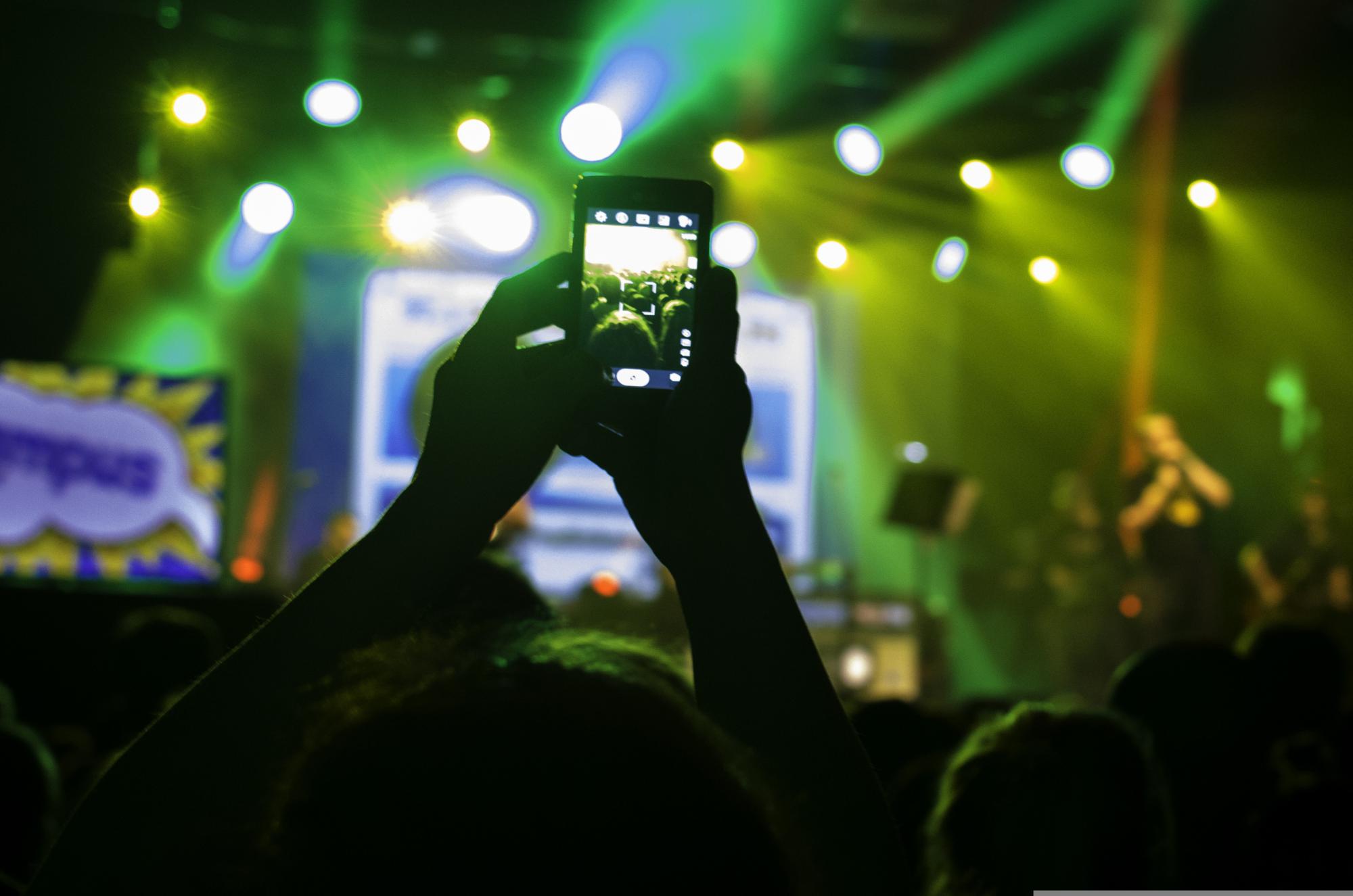 Op een concert steken mensen hun arm omhoog met hun toestel in de aanslag. Het nemen van foto’s vormt een nieuwe manier van aanwezig zijn. 