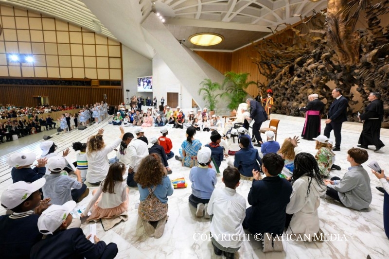 In de Paulus VI-zaal, waar kort voordien nog de synode over synodaliteit plaatsvond, nemen kinderen plaats op het podium rond paus Franciscus.