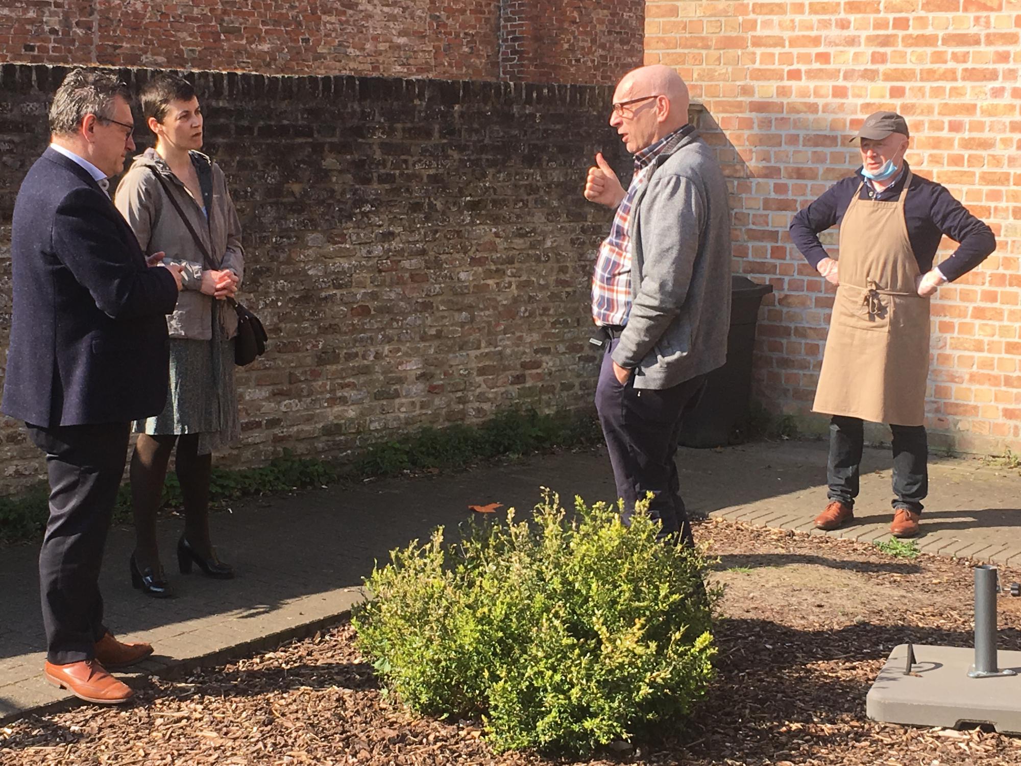 Priester Antoon Vandeputte geeft uitleg aan burgemeester Dirk De fauw en gemeenteraadslid Doenja Van Belleghem over de afhaalmaaltijden-actie van Open Balie